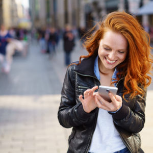 glückliche frau steht in der stadt und tippt auf ihrem handy