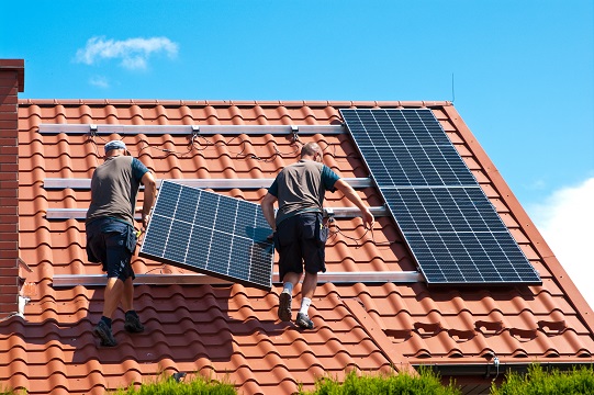 Two men installing new solar panels on the roof of a private house