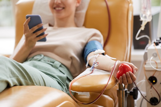 junge Frau mit Smartphone beim Blutspenden