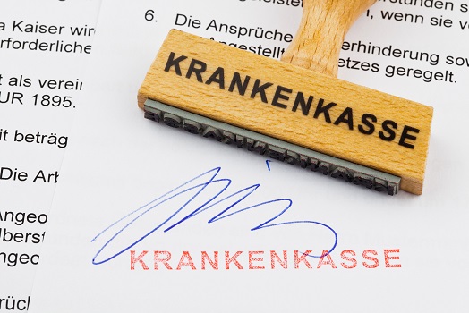 Ein Stempel aus Holz liegt auf einem Dokument. Deutsche Aufschrift: Krankenkasse