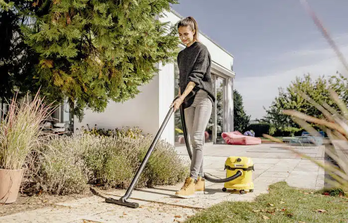 Frau saugt mit ihrem Kärcher WD 2 Plus V-12/4/18 C Nass- & Trockensauger draußen auf der Terrasse den Laub weg.