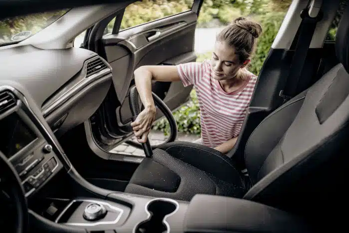 Frau saugt mit ihrem Kärcher WD 2 Plus V-12/4/18 C Nass- & Trockensauger die Autositze sauber.