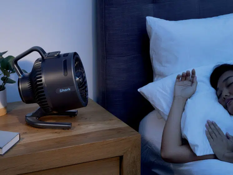 Frau schläft zum Shark Flex Breeze HydroGo Ventilator mit Sprühnebel.