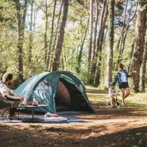 Bild von dreiköpfiger Familie im Wald am hellichten Tag mit dem Quechua MH100 XL Campingzelt in der Mitte.