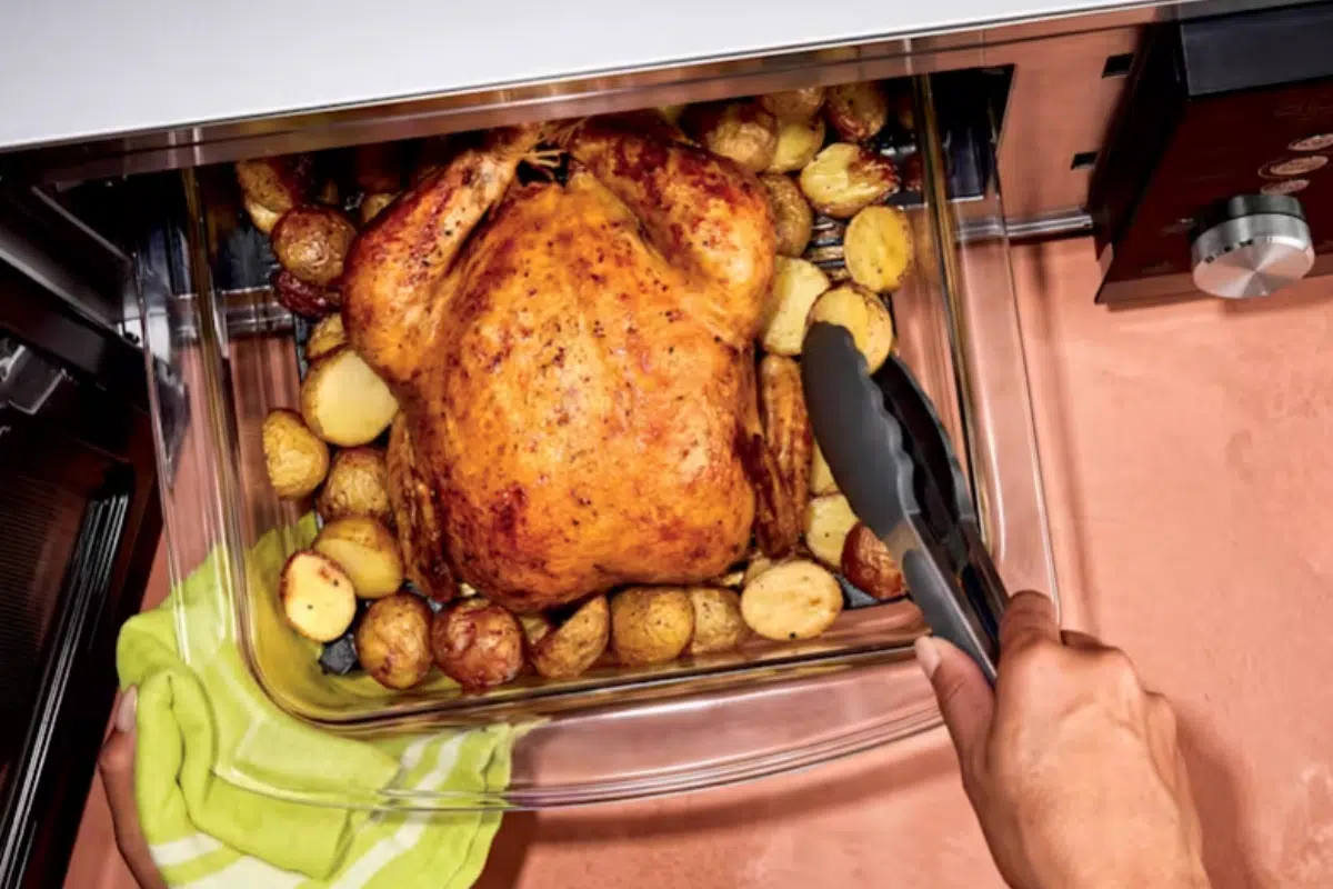 Ninja Crispi Microwave und Airfryer: Bei geöffneter Tür wird die große Glasform mit einem ganzen knusprigen Hähnchen auf Kartoffeln entnommen