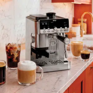Die neue Ninja Luxe Café MINI Plus ES352EU auf einer Küchen-Anrichte, daneben verschiedene Kaffee-Zubereitungen