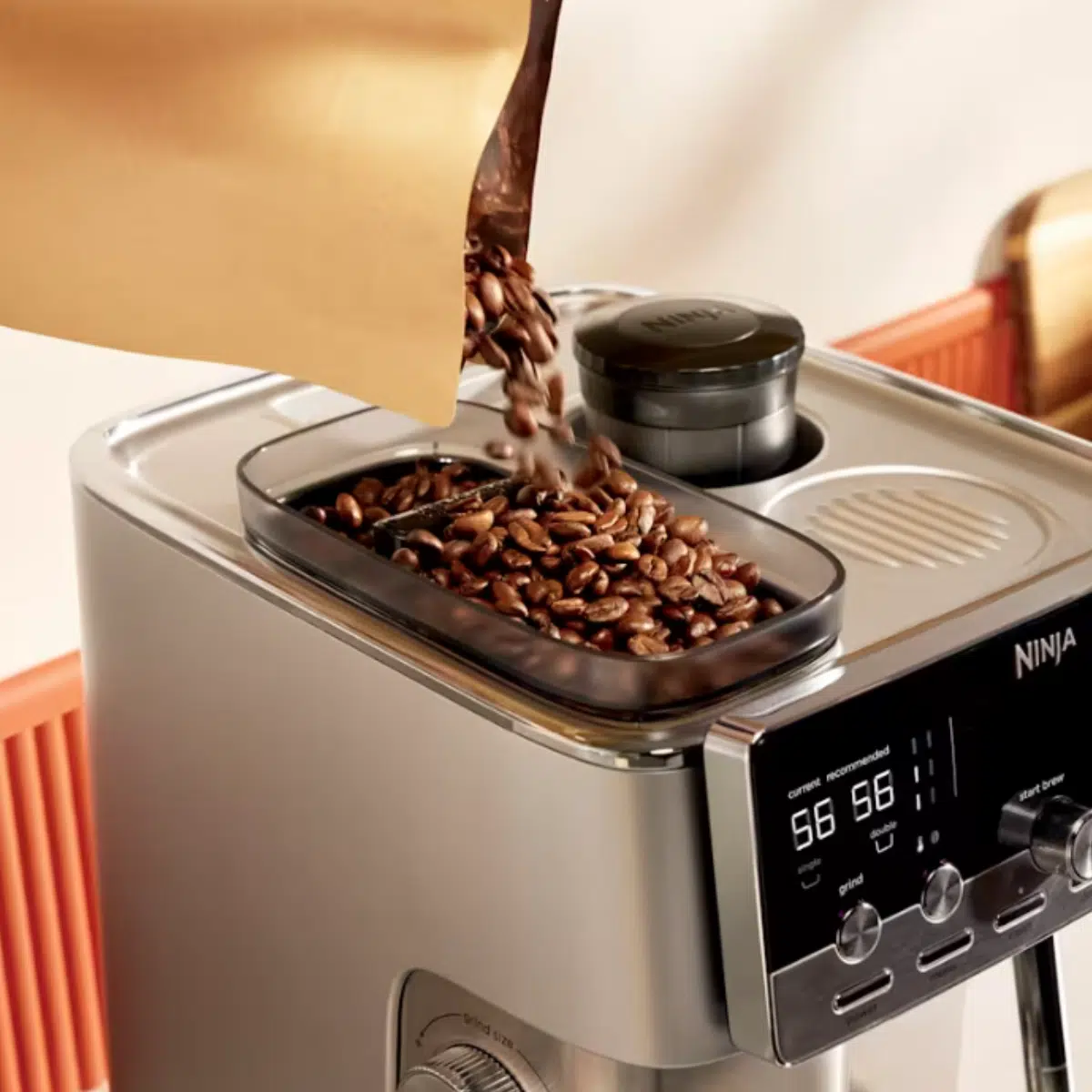 Die neue Ninja Luxe Café MINI Plus Kaffeemaschine von schräg oben: Kaffeebohnen werden aus einer Papiertüte ins Mahlwerk geschüttet