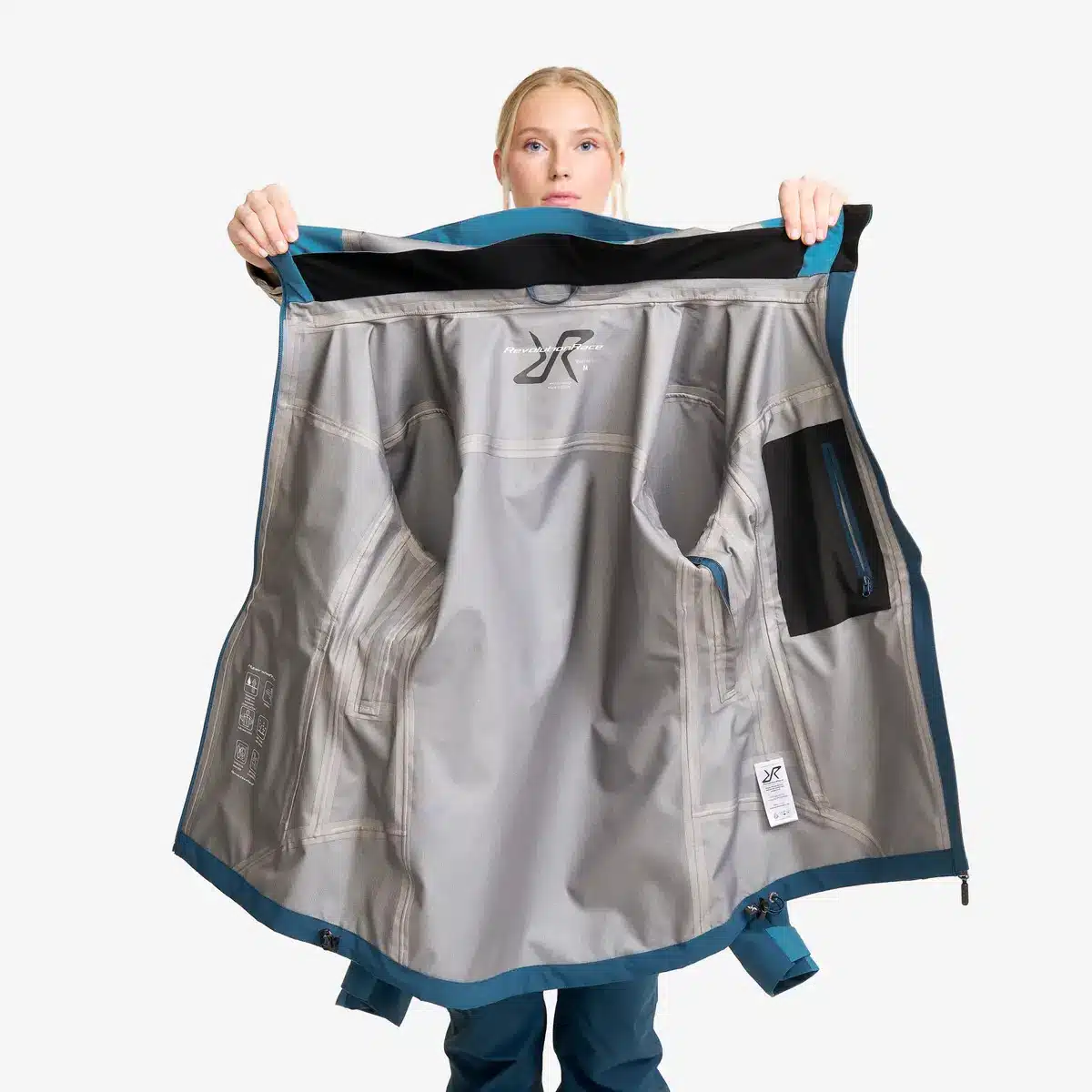 Dame hält die Innenseite der RevolutionRace Silence Proshell 3L Jacket Damen ausgebreitet in die Kamera